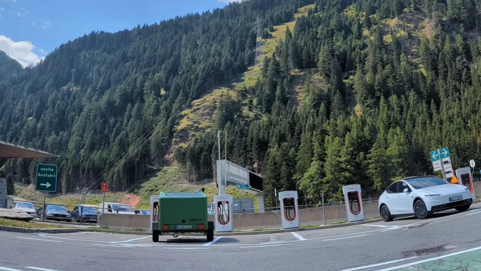 Wide-angle shot: the Glide and Tesla Model Y at the Supercharger on the Brenner Pass in front of wooded mountains