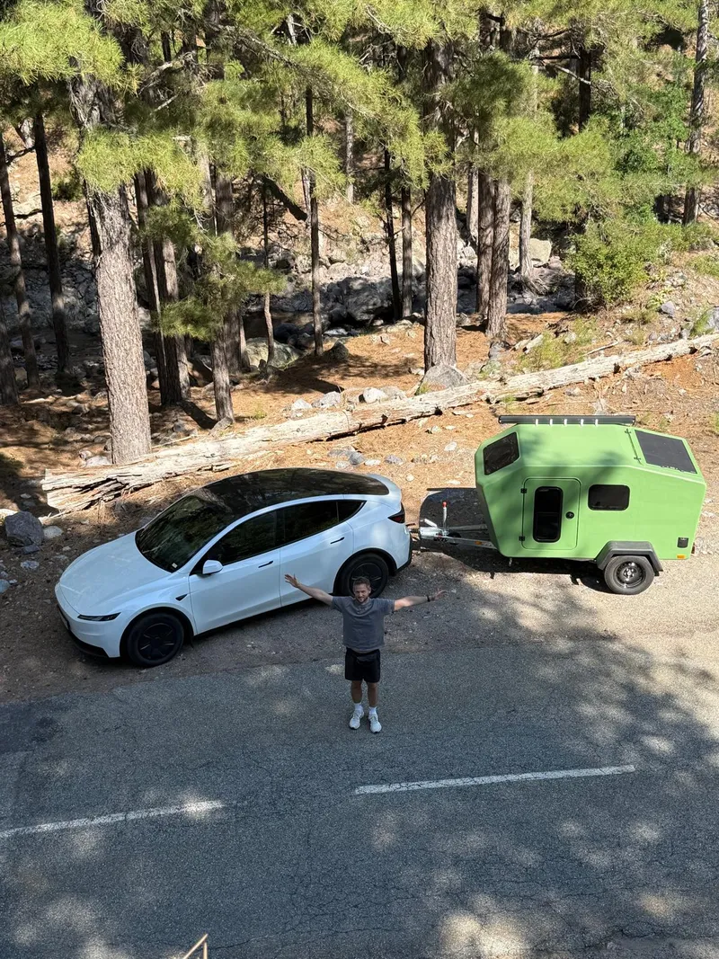 Drone shot: Tesla with the Glide in the pine forest, a person with outstretched arms in front
