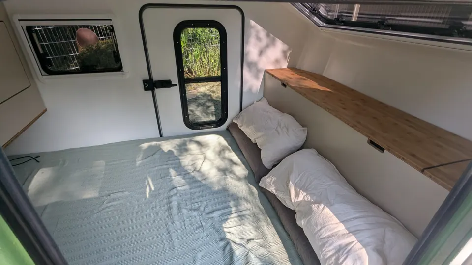 Bed with pillows, bamboo shelf, roof window and door with window inside