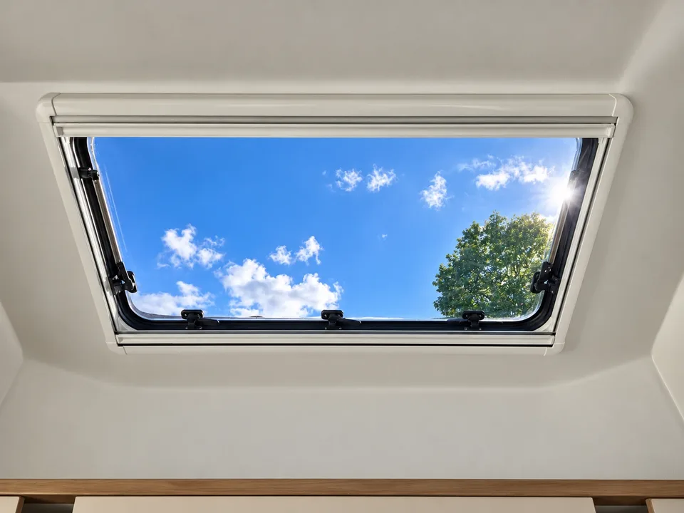 Open roof window with a view of the blue sky and a treetop