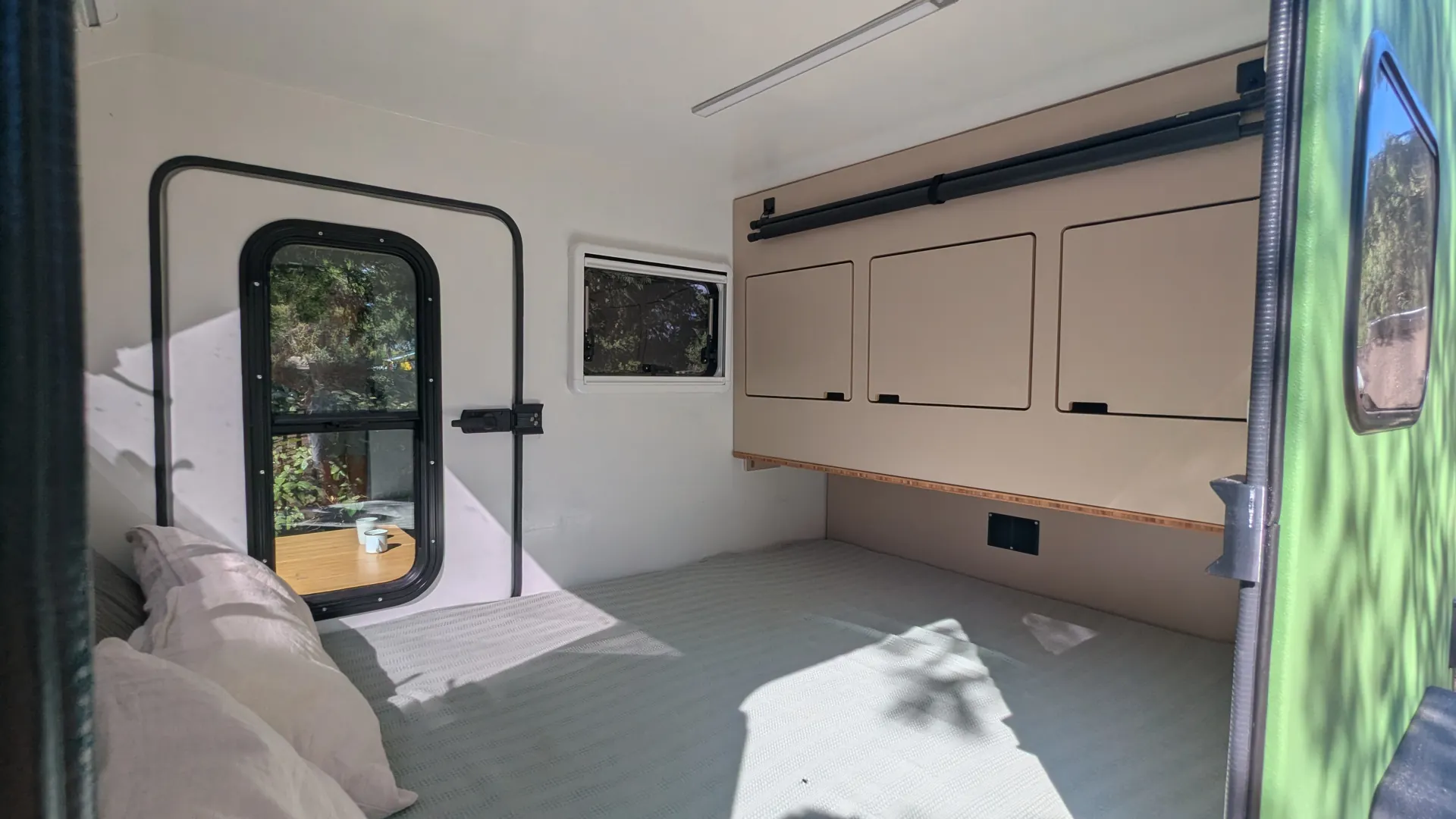 Bright interior of the Glide: large bed, built-in cabinet with three doors, side window and opposite door