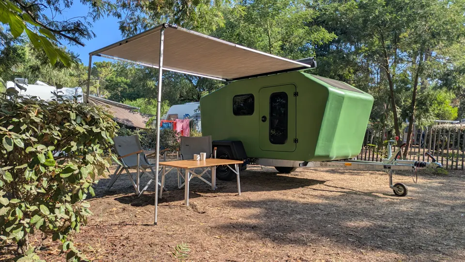 Green Glide with awning, chairs and bamboo table at a sunny campsite